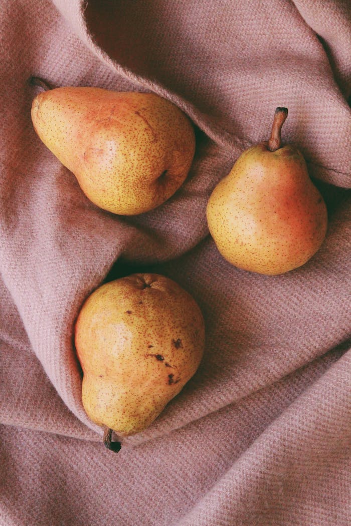 A cozy still life composition featuring ripe pears on a soft textile backdrop.